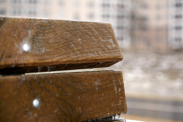 Wooden bench covered in glistening ice from freezing rain, showcasing intricate textures and details, with blurred background of urban environment creating a serene winter atmosphere