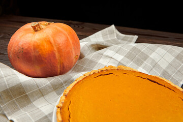 Fresh pumpkin beside a delicious pumpkin pie on a checkered cloth, showcasing autumn flavors and...