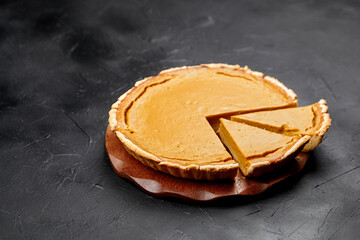 Delicious pumpkin pie on a wooden serving board, with a slice removed, showcasing a smooth filling and golden crust, perfect for autumn celebrations and festive gatherings