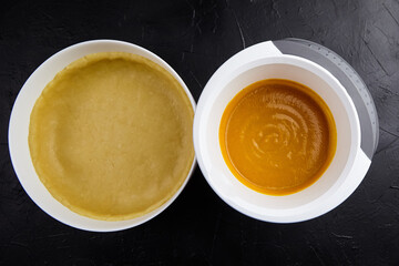 Pumpkin pie preparation with unbaked crust and spiced pumpkin filling in bowls on a dark textured surface, showcasing the baking process and ingredients for a delicious dessert