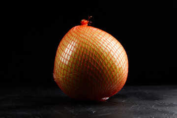 Pomelo fruit wrapped in bright orange netting, showcasing its round shape and smooth texture...