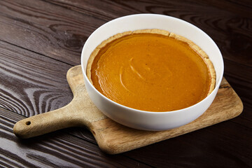Pumpkin pie in a white ceramic dish on a wooden cutting board, showcasing a smooth, rich filling and a golden crust, perfect for autumn celebrations and festive gatherings