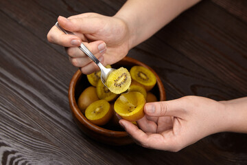 Hands holding a spoon, extracting slices of yellow fruit from a wooden bowl, showcasing the fresh...