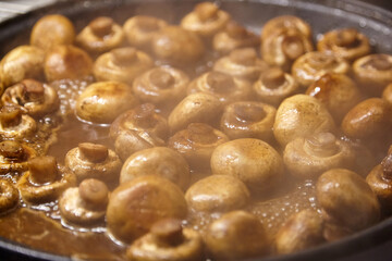 Fresh brown mushrooms are being sauteed in a skillet, surrounded by steam and rich sauce, showcasing the cooking process and delicious culinary preparation