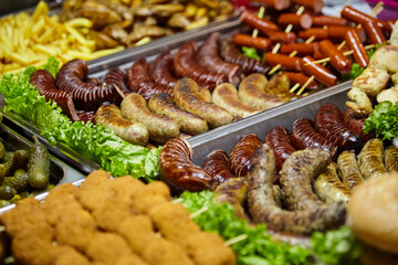 Assorted grilled sausages, crispy fries, and various meats arranged on trays with fresh lettuce, showcasing a vibrant food display for culinary enthusiasts and event catering
