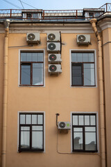 Facade of building with many air conditioners on windows in southern hot country. Yellow house exterior on city street. Escape from heat, creating favorable microclimate in urban apartments concept.