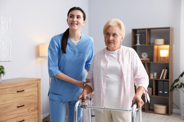 Nurse assisting senior woman with walking frame indoors. Home health care service