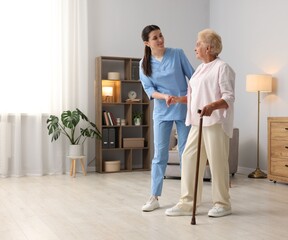 Nurse assisting senior woman with walking cane indoors, space for text. Home health care service