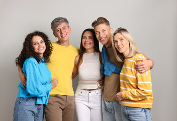 Group of happy friends hugging on grey background