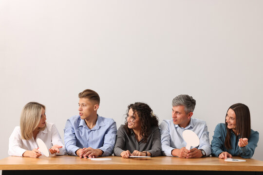 Panel of judges consulting at table against light grey background