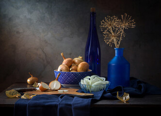 Contemporary still life with onions and blue dishes on a dark background