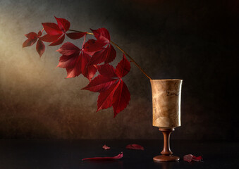 A laconic still life with an autumn branch of wild grapes in a wooden glass on a dark background