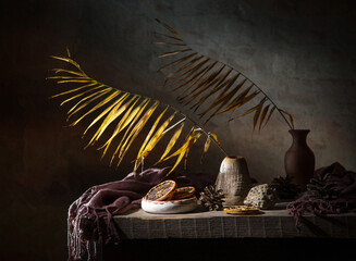 Still life with a dry palm branch in a clay vase and dried oranges on a dark background
