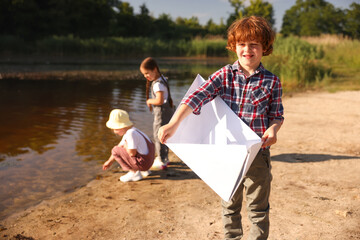 Children in nature, selective focus. Cute little boy with paper boat by lake