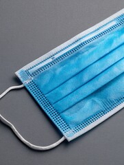 close-up, eye-level shot of a standard disposable medical face mask (surgical type) with its pleated texture clearly visible. The elastic ear loops are neatly folded, emphasizing its readiness 