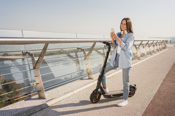 Full size of Caucasian woman using e-scooter and mobile phone searching right way on online map...