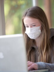 person wearing a medical face mask while working remotely on a laptop, in a home office setting. The scene conveys adaptability, safety, and the integration of masks into daily life. person, 