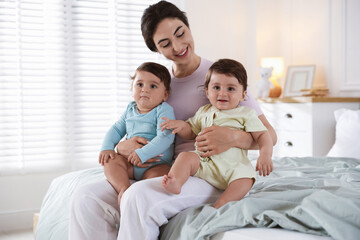 Happy mother with her cute little twin babies on bed indoors