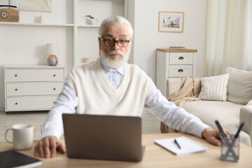 Fototapeta premium Senior man learning online using laptop at desk indoors. Self-study