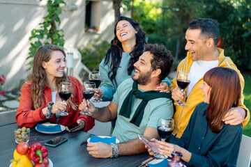 Group of young friends socializing and drinking red wine on a terrace during a summer aperitivo.