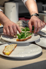 Chef preparing sandwich with arugula on rustic bread in professional kitchen