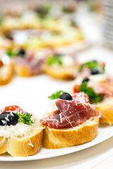 Close-up of Italian bruschetta with prosciutto, olives, cherry tomatoes, parsley, and grated cheese on toasted bread, served on a white plate