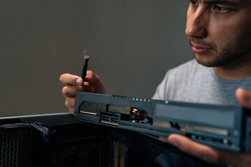 Portrait of young man meticulously cleaning graphics card with brush, performing essential...