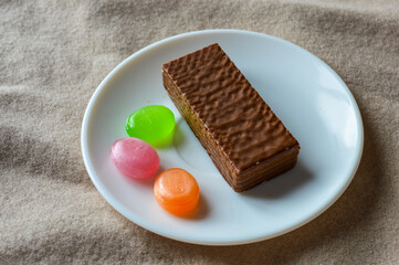 glass cup of black tea with a chocolate wafer and colorful hard candies on a white plate placed on...