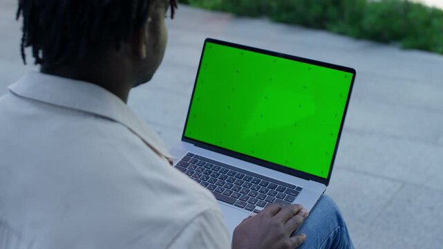 Man using laptop with green screen outdoors