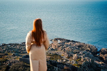 A woman is gazing thoughtfully at a scenic ocean view featuring a rocky shoreline