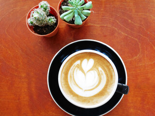 Beautiful Coffee Cup with Latte Art Surrounded by Small Potted Cactus Plants on Wooden Table