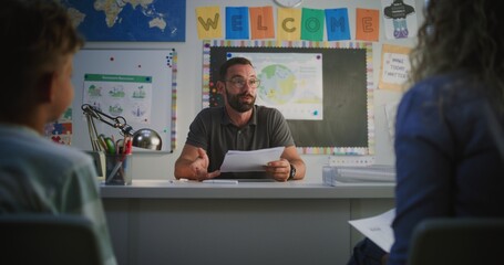 Male Teacher Giving School Test Results of Elementary School Student to His Mother. Teacher Praising Boy for High Grades and Academic Success. Parents Evening to Support Child's Learning. Dolly Shot.