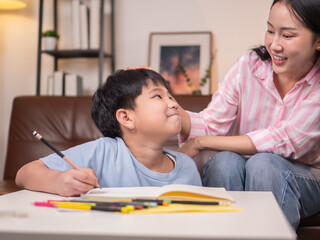 An Asian mother is helping her son do his homework in the living room.