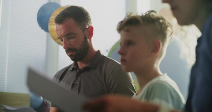 Parents Looking at School Exam Grades of Their Son in Classroom. Parents Upset About Poor School Performance of Primary School Student. Meeting to Support Child's Development. Slow Motion. Close Up.