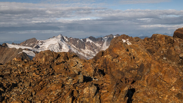 Rocky mountain landscape with snow-capped peaks in the distance under a cloudy sky. View from the top  of Vioz Mount, Trentino.