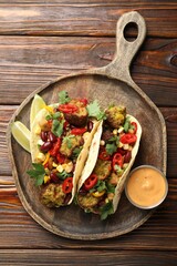 Tasty vegetarian tacos with falafel served with sauce on wooden table, top view