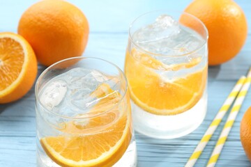 Sparkling water with orange slices in glasses, fresh fruits and straws on light blue wooden table, closeup