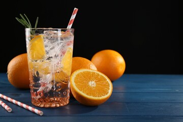 Sparkling water with orange in glass, fresh fruits and straws on blue wooden table, closeup. Space for text
