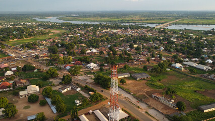 Aerial Panorama of Rural African Town with River, Bridge, and Red and White Tower.