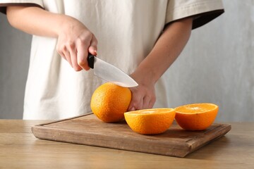 Making juice. Woman cutting orange at wooden table, closeup