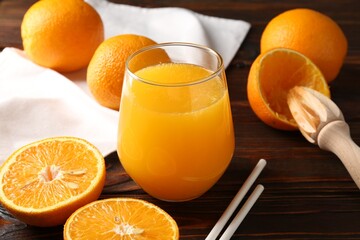 Fresh orange juice in glass, fruits, straws and juicer on wooden table, closeup