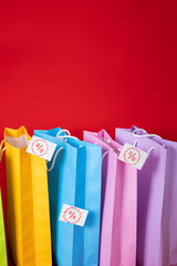 Multi colored shopping bags, with various discount percentage tags on a red background, sale...