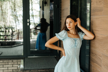 A woman in a blue dress stands near the wall and looks away