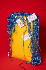 Yellow shopping bag with overflowing blue confetti and discount percentage tags on a red...