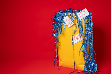 Yellow shopping bag with overflowing blue confetti and discount percentage tags on a red...