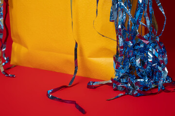 Close up of yellow shopping bag with blue confetti overflowing on a red background, shopping...
