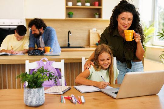Family enjoying time together doing homework and homeschooling with computer while mother drinks coffee