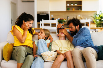 Family watching a scary movie on tv, father covering son's eyes