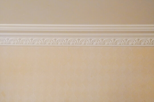 Elegant white crown molding with an ornate classical pattern against a beige painted wall.