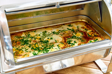 A beautifully cooked dish served in a gleaming chafing dish with fresh herbs and spices, showcasing...
